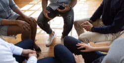 Adults on chairs sitting in a circle with their hands on their laps. Image is focussed on there laps and their faces are not visible.