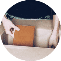 A person placing a brown book in a cardboard box