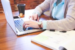 Hands typing on a computer, with an open book to one side and a coffee cup on the other.